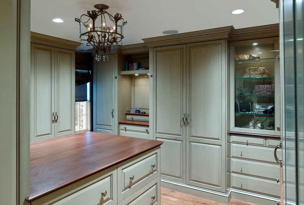 Luxurious walk-in closet with paneled cabinetry, a central storage island, wood countertops, glass display cabinets, and a decorative chandelier.