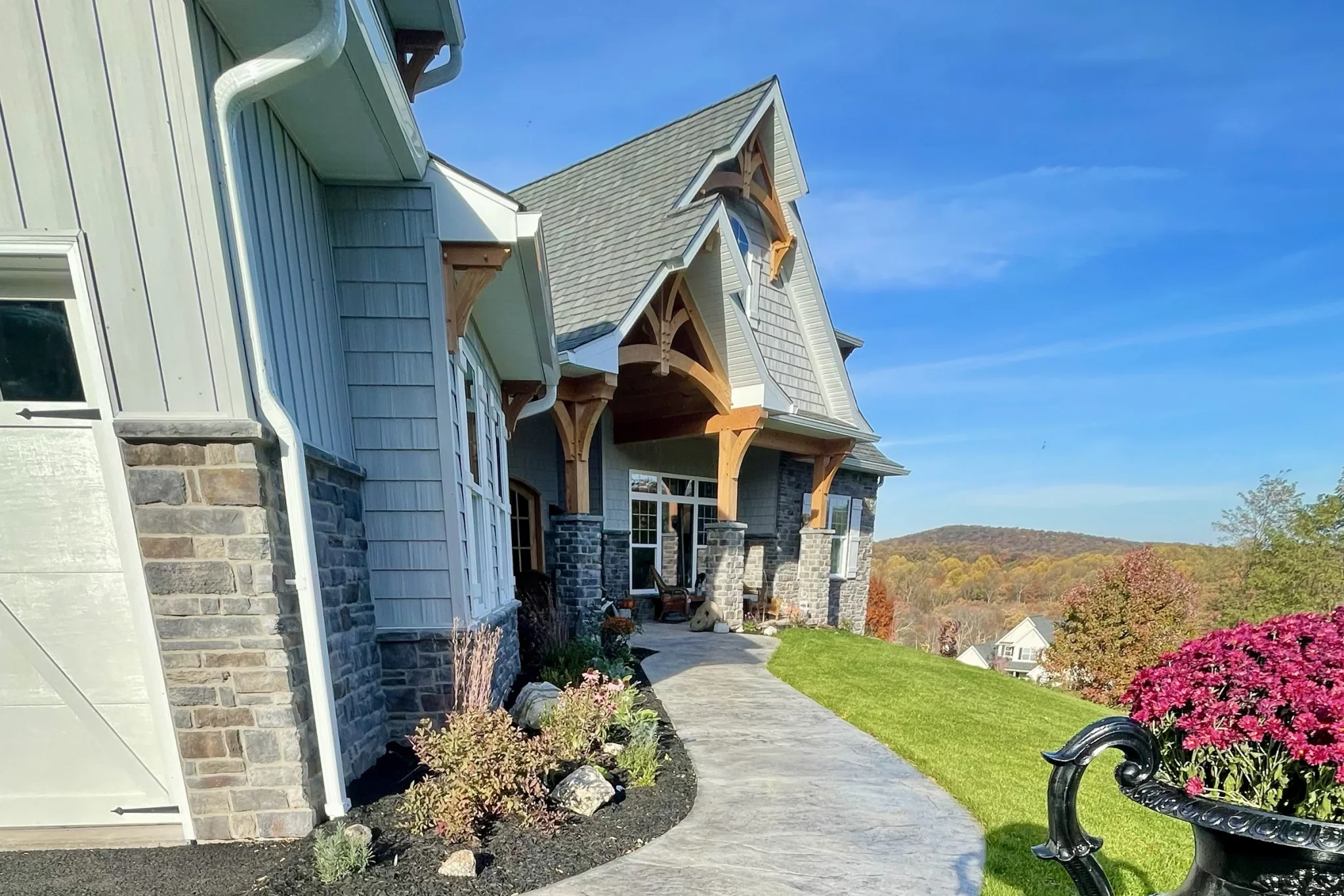 Front view of a custom craftsman-style home in Wyomissing, PA with stone and shingle siding, timber frame entry, and panoramic hillside backdrop.