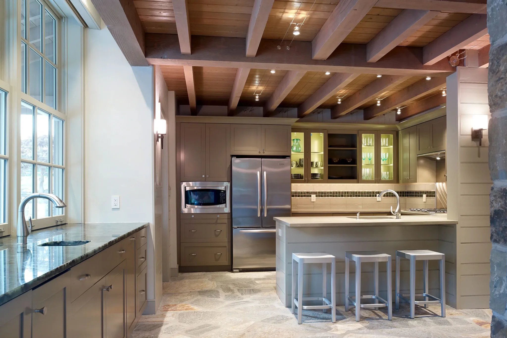 Custom built-in window bench with storage drawers, upholstered seat cushions, and decorative throw pillows beneath a large set of windows with a scenic outdoor view.