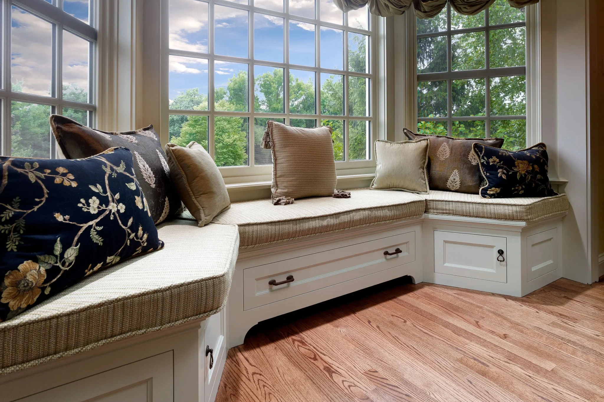 Custom built-in window seat with storage drawers and decorative throw pillows in a sunlit home design in Wyomissing, PA.
